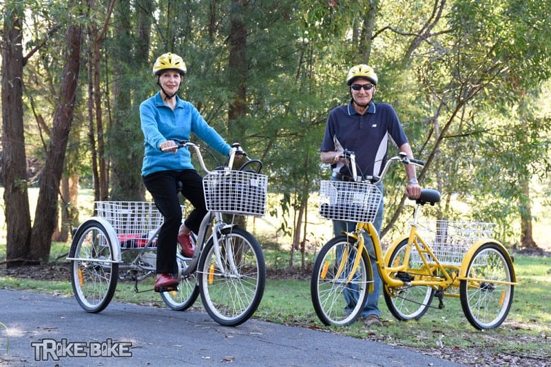Couple riding adult tricycles on Australian bike path Man and woman riding tricycles with baskets on a path