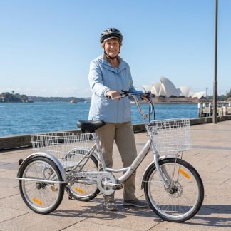 A senior woman standing with a silver adult tricycle with a white basket, perfect for disability mobility and casual rides.