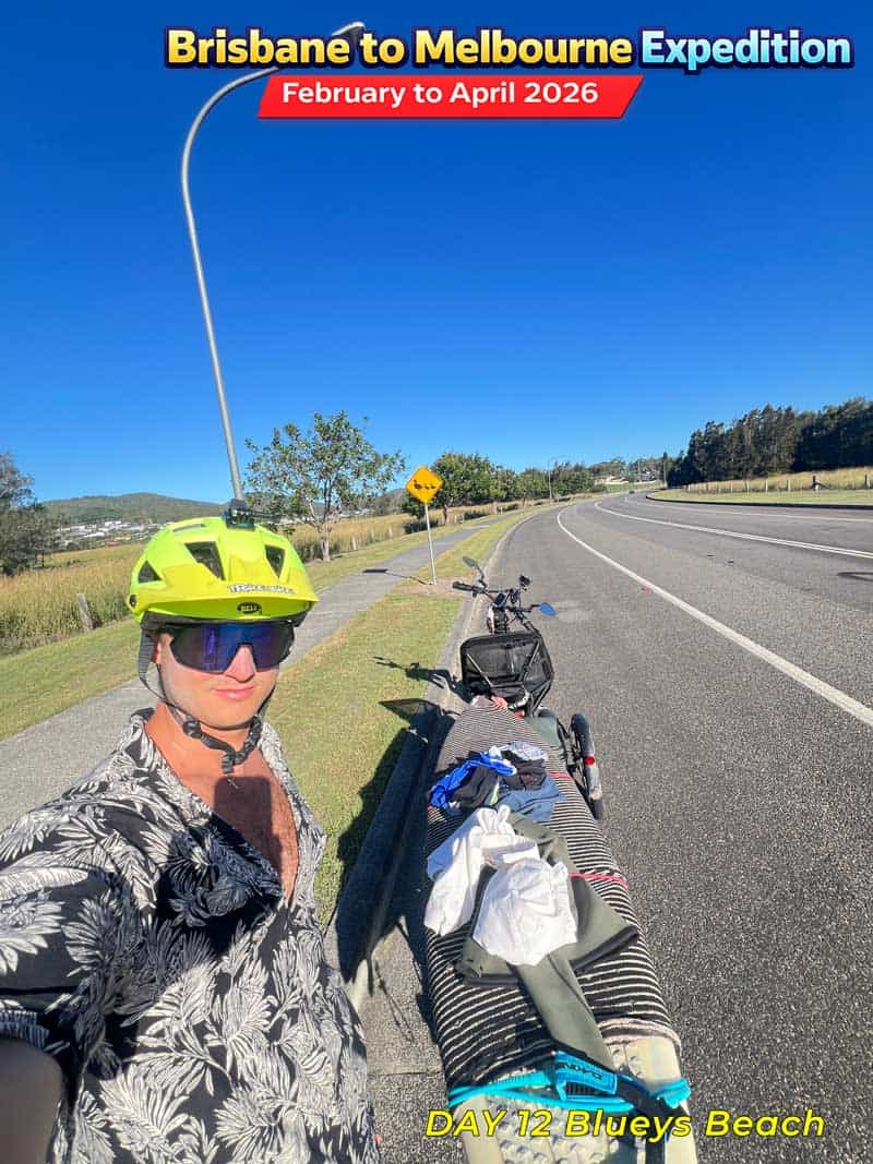 A person riding an adult tricycle on a highway in Australia, wearing a helmet and sunglasses. The tricycle is loaded with luggage.
