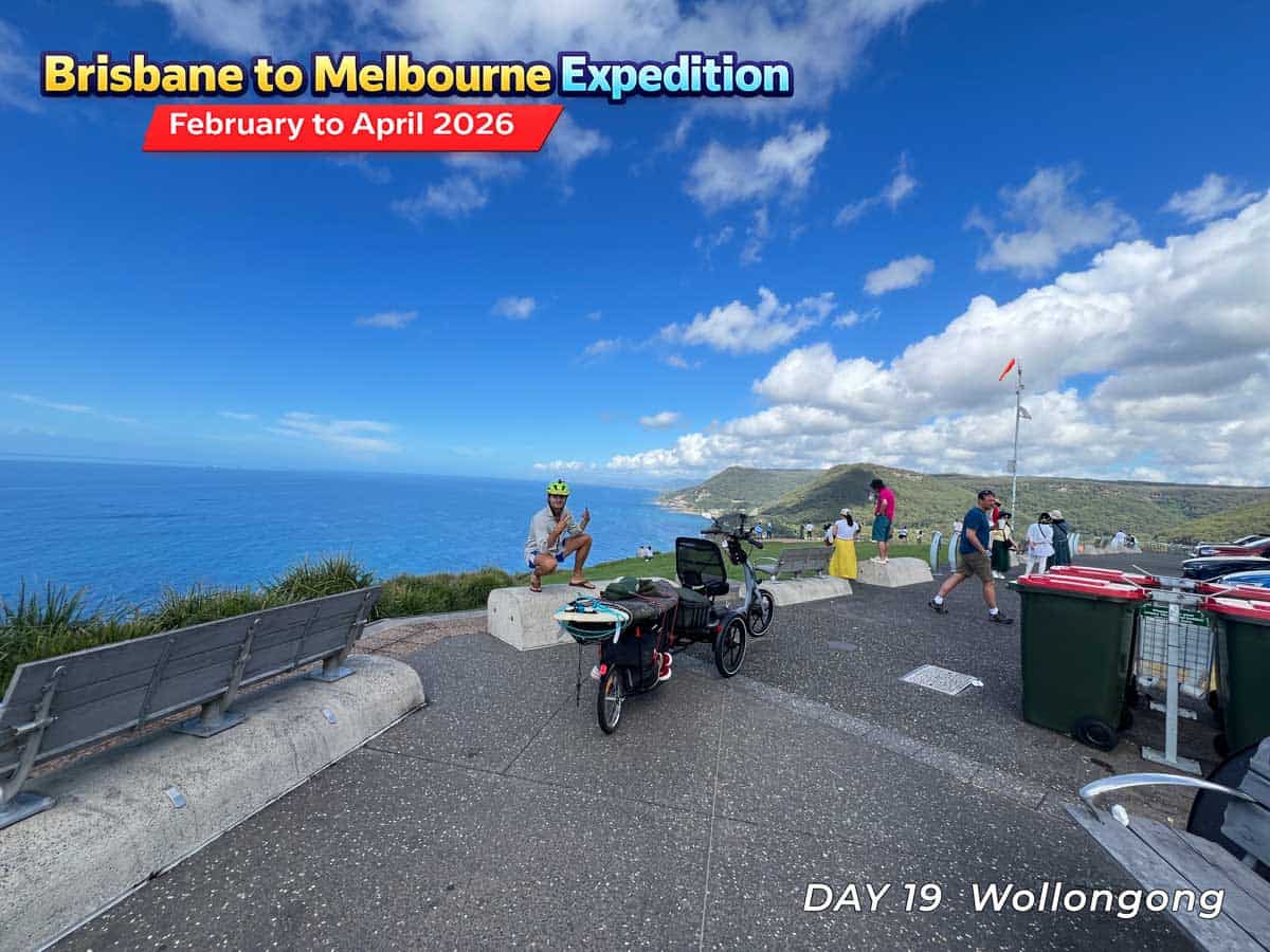 A senior riding an adult tricycle on a scenic coastal road in Australia. The tricycle has a large seat and basket.