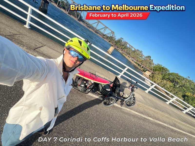 A person riding an adult tricycle on a road in Australia. The tricycle has a red seat.