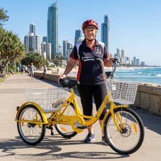 A senior woman on a yellow tricycle with a basket on a beachside path. The tricycle features a sturdy design suitable for adult riders.