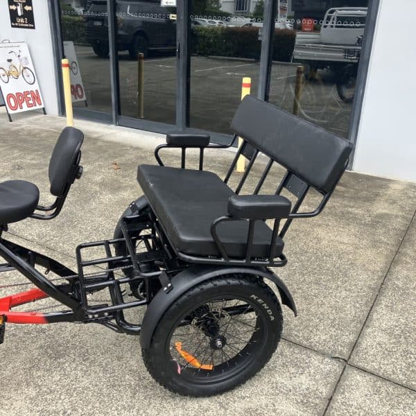 Red Electric Adult Tandem Tricycle for Two A red and black electric tandem tricycle with two seats and a large rear wheel. Designed for adult riders.